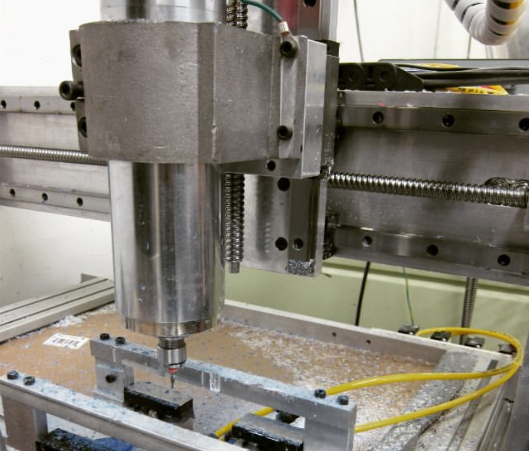 Close-up of a CNC milling machine spindle and bit positioned over a workpiece clamped to the machine bed.